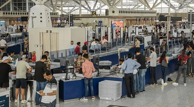 Airport security screening area with passengers, staff, and baggage scanners