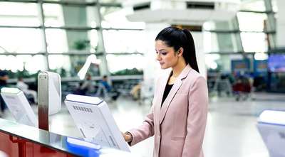 Woman using a self-service check-in kiosk inside an airport terminal.