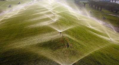 Water sprinklers irrigating large green lawn